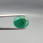 "Natural Emerald Panna Zamrud gemstone 4.82 carat oval cut from Zambia held in tweezers showing deep green color and natural jardin inclusions"