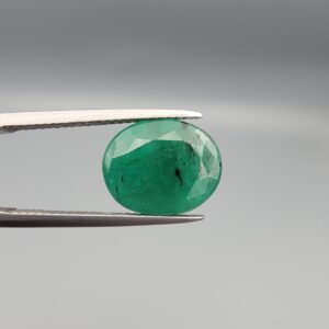 "Natural Emerald Panna Zamrud gemstone 4.82 carat oval cut from Zambia held in tweezers showing deep green color and natural jardin inclusions"