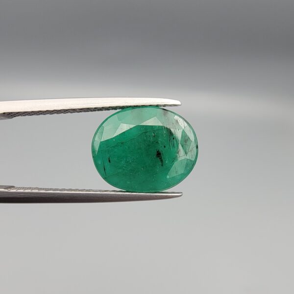 "Natural Emerald Panna Zamrud gemstone 4.82 carat oval cut from Zambia held in tweezers showing deep green color and natural jardin inclusions"