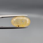 "Natural unheated Yellow Sapphire Pukhraj gemstone 10.60 carat large oval cut from Sri Lanka Ceylon held in tweezers showing golden color and visible natural fractures"