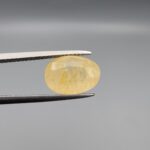 "Natural unheated Yellow Sapphire Pukhraj gemstone 6.37 carat large oval cut from Sri Lanka Ceylon held in tweezers showing pale golden color and natural feather inclusions"