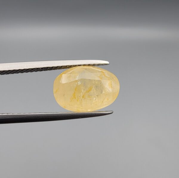 "Natural unheated Yellow Sapphire Pukhraj gemstone 6.37 carat large oval cut from Sri Lanka Ceylon held in tweezers showing pale golden color and natural feather inclusions"