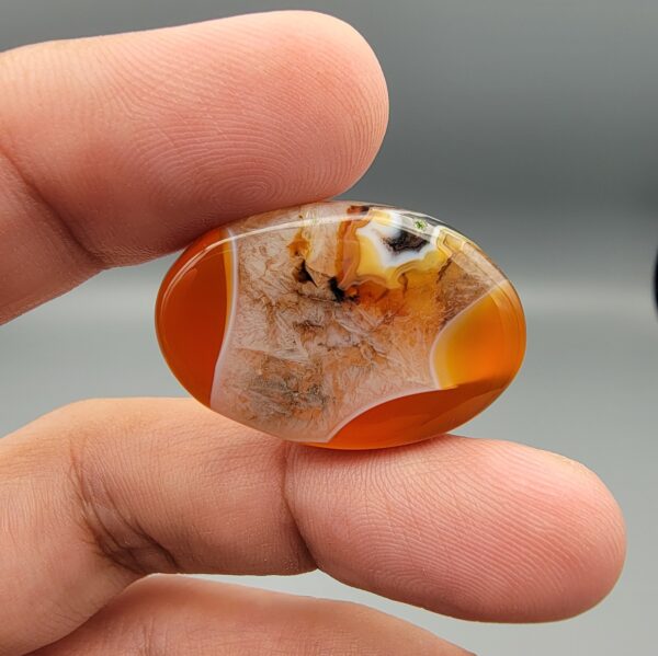 "Natural Carnelian Agate gemstone 85.42 carat oval cabochon from Yemen displayed in jewelry box showing red, orange, yellow, white, and brown natural color zones"