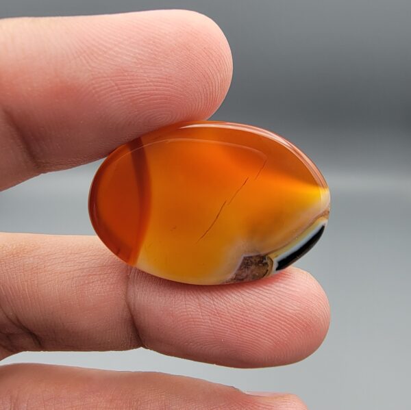 "Natural Carnelian Agate gemstone 85.42 carat oval cabochon from Yemen displayed in jewelry box showing red, orange, yellow, white, and brown natural color zones"