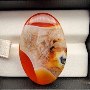 "Natural Carnelian Agate gemstone 85.42 carat oval cabochon from Yemen displayed in jewelry box showing red, orange, yellow, white, and brown natural color zones"