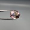 ​A precision-faceted 5.36-carat oval natural Ametrine gemstone held in tweezers against a gray backdrop, displaying a sharp half-and-half color partition of purple amethyst and golden-amber citrine with brilliant clarity.