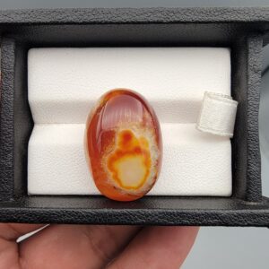 "Natural Carnelian Banded Agate Sulemani Aqeeq gemstone 32.29 carat oval cabochon from Yemen held in tweezers showing red, orange, yellow, and white natural color bands"