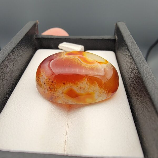"Natural Carnelian Banded Agate Sulemani Aqeeq gemstone 32.29 carat oval cabochon from Yemen held in tweezers showing red, orange, yellow, and white natural color bands"