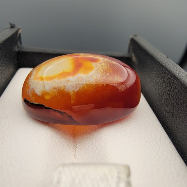 "Natural Carnelian Banded Agate Sulemani Aqeeq gemstone 32.29 carat oval cabochon from Yemen held in tweezers showing red, orange, yellow, and white natural color bands"