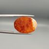 ​An 18.40-carat oval natural Yemeni carnelian agate cabochon held in tweezers against a gray studio background. One face displays a crystalline white-and-red frost matrix edged in bright yellow-orange, while the reverse side reveals a glowing field of carnelian red and orange botryoidal cloud patterns.