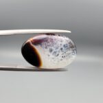 A rare 13.15 carat oval cabochon of natural Sulemani Aqeeq from Iran, pairing a classic black-and-orange banded edge with a sparkling druzy quartz crystal window flushed with deep maroon inclusions — a true collector's specimen that stands apart from typical solid black Sulemani stones.