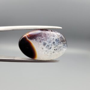 A rare 13.15 carat oval cabochon of natural Sulemani Aqeeq from Iran, pairing a classic black-and-orange banded edge with a sparkling druzy quartz crystal window flushed with deep maroon inclusions — a true collector's specimen that stands apart from typical solid black Sulemani stones.