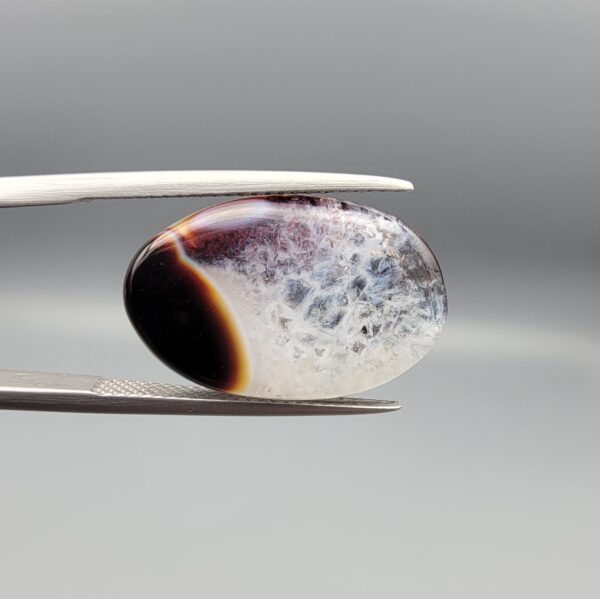 A rare 13.15 carat oval cabochon of natural Sulemani Aqeeq from Iran, pairing a classic black-and-orange banded edge with a sparkling druzy quartz crystal window flushed with deep maroon inclusions — a true collector's specimen that stands apart from typical solid black Sulemani stones.