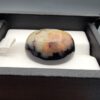 ​A 33.48-carat oval natural Iranian chalcedony agate cabochon displayed in a black presentation box. The high dome features translucent milky agate with multi-colored dendritic inclusions, mossy specks, and geode crystal pocket formations, backed by a seamless, shining jet-black base.