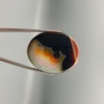 A large 64.07 carat oval cabochon of natural Sulemani Aqeeq from Iran, its front face showing a dramatic black-and-cream orbicular "bubble" formation, while the reverse glows in layered amber, rust, and burgundy rings — a true two-faced statement stone with rare orbicular texture on both sides.