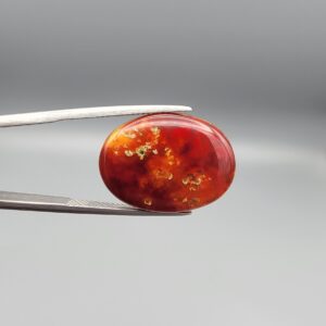 "Natural Irani Fire Agate Sulemani Aqeeq gemstone 16.65 carat oval cabochon from Iran held in tweezers showing deep red and orange color with natural cavity eye inclusions and green moss spots"