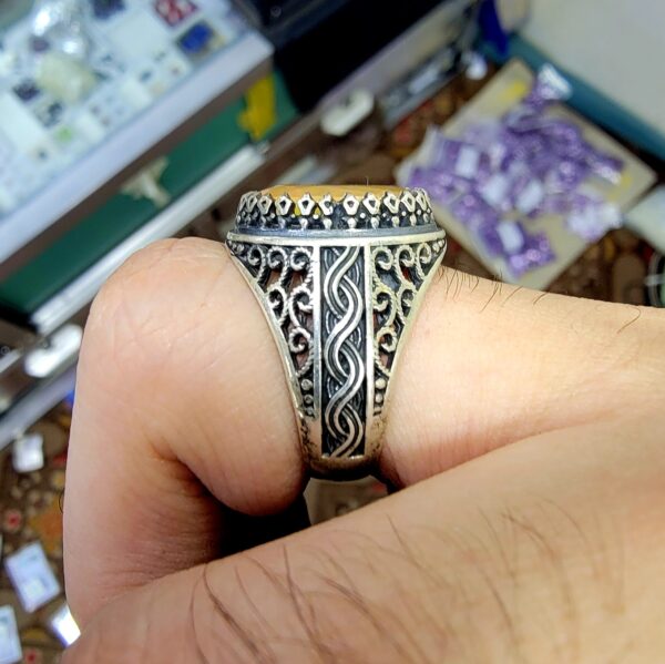Hand-worn view of a men's Turkish design 925 sterling silver ring featuring a large 4 carat plus oval yellow-orange natural Ethiopian opal gemstone with intricate side band filigree.