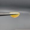 Studio photograph held in steel tweezers showcasing a 5.79 carat natural oval-shaped Ethiopian opal loose gemstone with a double-side fancy cut featuring flat and domed facets.