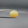 Studio photograph held in steel tweezers showcasing a 5.79 carat natural oval-shaped Ethiopian opal loose gemstone with a double-side fancy cut featuring flat and domed facets.