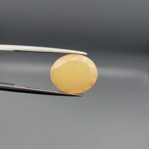 Studio photograph held in steel tweezers showcasing a 4.05 carat natural oval-shaped Ethiopian opal loose gemstone featuring a double-side fancy cut with flat and domed facets.