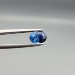Studio photograph of a 1.13 carat natural oval-shaped blue sapphire loose gemstone displaying deep blue facets and authentic surface cavities.