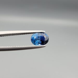 Studio photograph of a 1.13 carat natural oval-shaped blue sapphire loose gemstone displaying deep blue facets and authentic surface cavities.