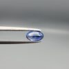 ​Studio close-up photograph of a 0.91 carat natural oval-shaped blue sapphire loose gemstone resting on a textured white surface, showcasing blue facets and a shiny finish.