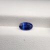 ​Studio close-up photograph of a 0.91 carat natural oval-shaped blue sapphire loose gemstone resting on a textured white surface, showcasing blue facets and a shiny finish.