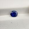Studio photograph held in steel tweezers showcasing a 1.14 carat natural oval-shaped blue sapphire loose gemstone with deep blue facets and a high-shine finish.