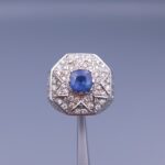 Studio close-up photograph of a handcrafted 925 sterling silver men's ring featuring a central 2+ carat blue sapphire surrounded by a geometric star design pavé-set with natural diamonds.