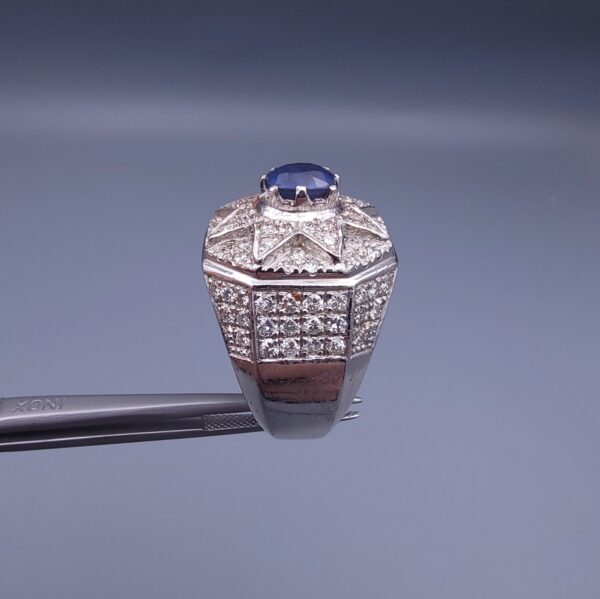 Studio close-up photograph of a handcrafted 925 sterling silver men's ring featuring a central 2+ carat blue sapphire surrounded by a geometric star design pavé-set with natural diamonds.