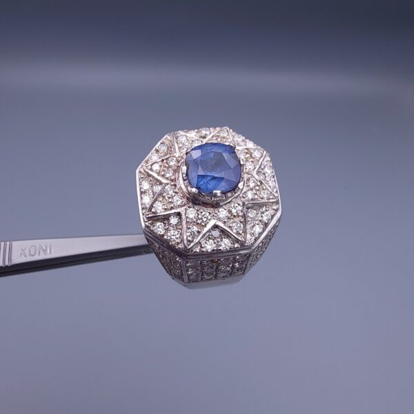 Studio close-up photograph of a handcrafted 925 sterling silver men's ring featuring a central 2+ carat blue sapphire surrounded by a geometric star design pavé-set with natural diamonds.