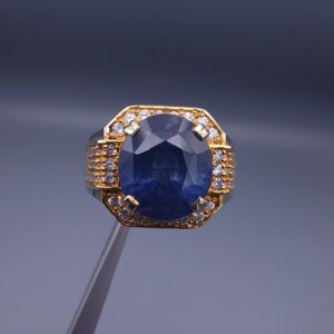 Studio close-up photograph of a handcrafted size 21 men's two-tone 925 sterling silver ring featuring a 4+ carat oval blue sapphire center stone surrounded by sparkling artificial zircons.