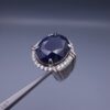 Studio close-up photograph of a handcrafted men's 925 sterling silver ring featuring a massive 19.72 carat oval blue sapphire center stone surrounded by a zircon halo and detailed with seven carved wheel motifs along the shank.