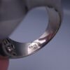 Studio close-up photograph of a handcrafted men's 925 sterling silver ring featuring a massive 19.72 carat oval blue sapphire center stone surrounded by a zircon halo and detailed with seven carved wheel motifs along the shank.
