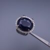 Studio close-up photograph of a handcrafted men's 925 sterling silver ring featuring a massive 19.72 carat oval blue sapphire center stone surrounded by a zircon halo and detailed with seven carved wheel motifs along the shank.