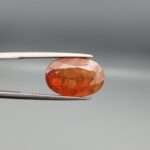 Studio close-up photographs showing the front and back view of a 10.74 carat oval-cut natural hessonite garnet gemstone displaying a warm honey-orange color and semi-transparent clarity.