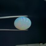 Studio close-up photograph of an 8.48 carat oval cabochon natural Ethiopian Welo opal showcasing a vibrant green, red, and yellow play-of-color against a dark background.