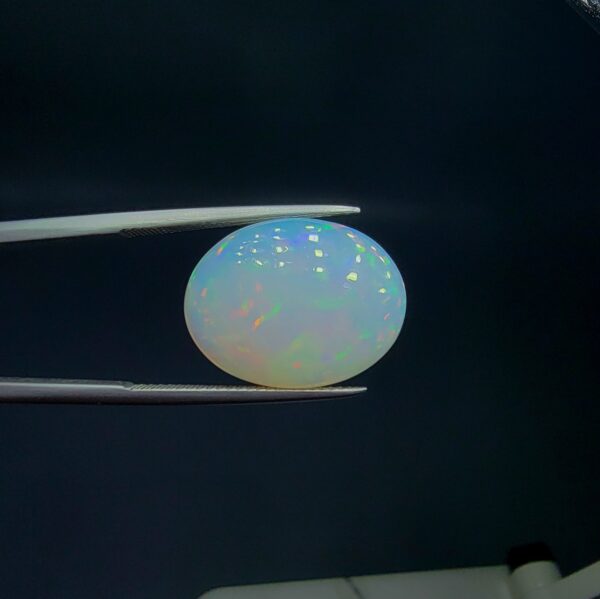 Studio close-up photograph of an 8.48 carat oval cabochon natural Ethiopian Welo opal showcasing a vibrant green, red, and yellow play-of-color against a dark background.