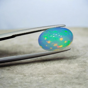 Studio close-up photograph of a 4.16 carat oval cabochon natural Ethiopian Welo opal displaying vibrant green, red, and yellow play-of-color held by tweezers.