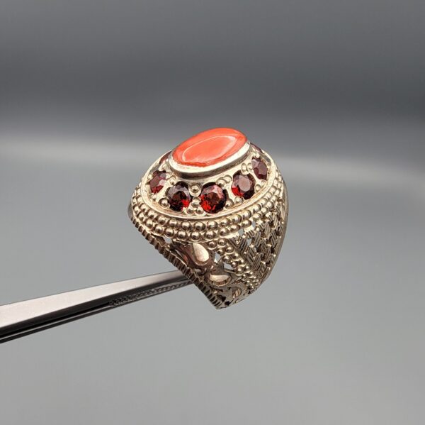 Studio close-up photographs showing the top and side profile views of a handcrafted size 23 solid 925 sterling silver ring featuring a natural Italian coral center stone surrounded by faceted garnet accent stones.