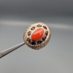 Studio close-up photographs showing the top and side profile views of a handcrafted size 23 solid 925 sterling silver ring featuring a natural Italian coral center stone surrounded by faceted garnet accent stones.