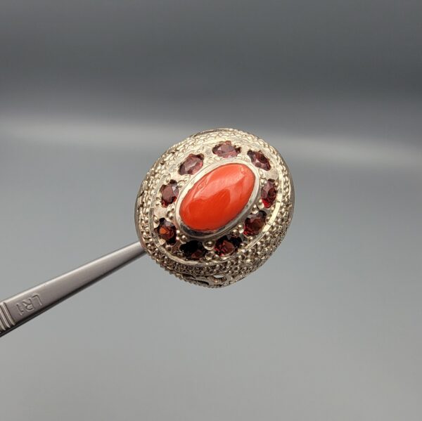 Studio close-up photographs showing the top and side profile views of a handcrafted size 23 solid 925 sterling silver ring featuring a natural Italian coral center stone surrounded by faceted garnet accent stones.