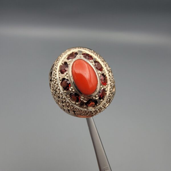 Studio close-up photographs showing the top and side profile views of a handcrafted size 23 solid 925 sterling silver ring featuring a natural Italian coral center stone surrounded by faceted garnet accent stones.