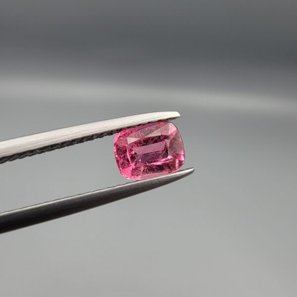 Studio close-up photographs showing the top and facet profile views of a 0.63 carat cushion mixed cut natural rubellite tourmaline loose gemstone held in tweezers.