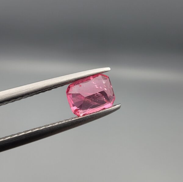 Studio close-up photographs showing the top and facet profile views of a 0.63 carat cushion mixed cut natural rubellite tourmaline loose gemstone held in tweezers.