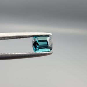 Studio close-up photographs showing the top and facet profile views of a 0.51 carat cushion cut natural blue tourmaline loose gemstone held in precision tweezers.