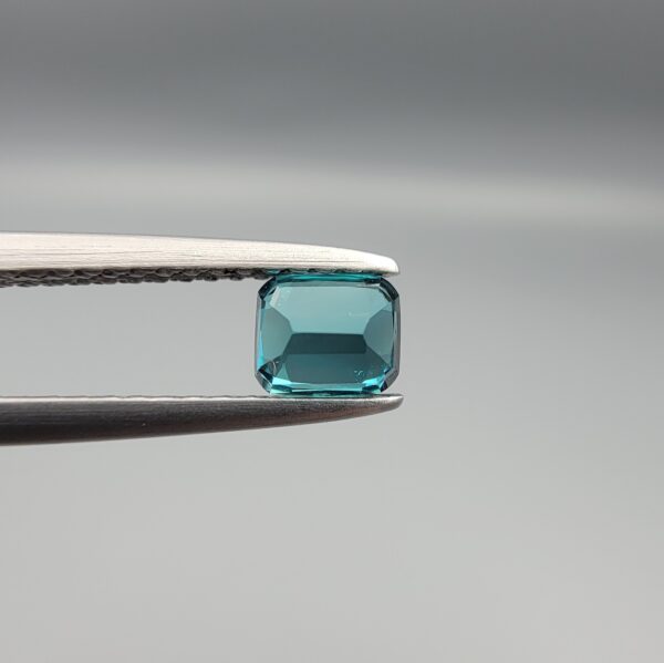 Studio close-up photographs showing the top and facet profile views of a 0.51 carat cushion cut natural blue tourmaline loose gemstone held in precision tweezers.