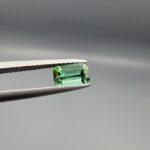 Studio close-up photographs showing the top and facet profile views of a 0.94 carat octagon cut natural blue tourmaline loose gemstone held in precision tweezers.