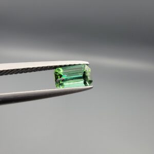 Studio close-up photographs showing the top and facet profile views of a 0.94 carat octagon cut natural blue tourmaline loose gemstone held in precision tweezers.